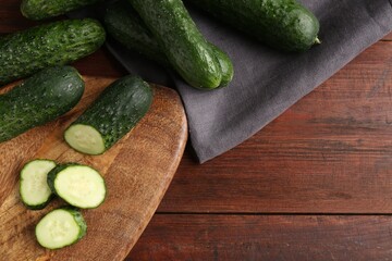 Whole and cut cucumbers on wooden table, flat lay. Space for text