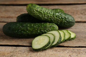 Whole and cut cucumbers on wooden table, closeup
