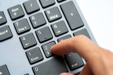 Closeup macro view of human hand pressing number two key on numeric keypad of a computer keyboard, office data entry concept, finger interacting with numpad buttons accounting job work calculations