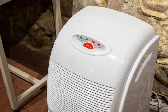 Basement room air dehumidifier appliance closeup white portable home device for humidity control and moisture removal purifier unit with vent grille operating in damp interior no people simple concept