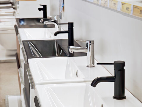 Row of modern bathroom sinks with black and chrome faucets on showroom display white ceramic basins and mixer taps in retail store sanitary ware selection for home renovation and interior design ideas