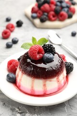 Tasty panna cotta with berries and jam on light grey table, closeup