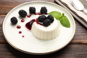Tasty panna cotta with blackberries, mint and sauce on wooden table, closeup