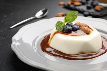 Tasty panna cotta with blueberries, almonds and sauce on black table, closeup
