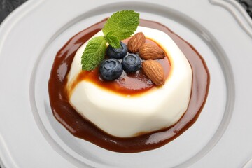 Tasty panna cotta with blueberries, almonds and sauce on plate, closeup