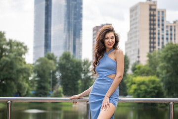 Young beautiful brunette woman in blue knitted dress posing in summer park