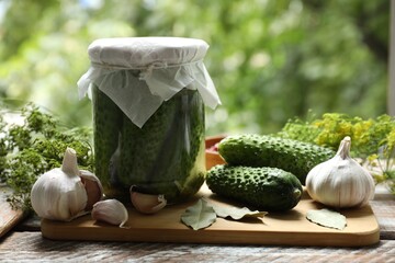 Making pickles. Fresh cucumbers in jar and spices on wooden table outdoors, closeup