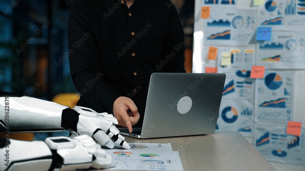 Poster a man interacts with a laptop while a robotic arm rests on the table, surrounded by various business