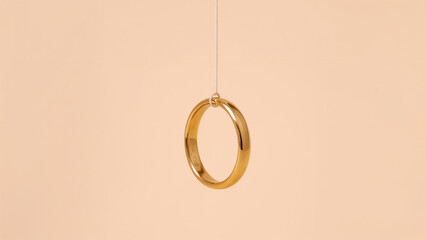 Single Gold Wedding Ring Suspended by Thin Thread Against Peach Background marriage