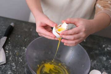 Young child focuses on cracking eggs into a mixing bowl, surrounded by baking tools and ingredients...