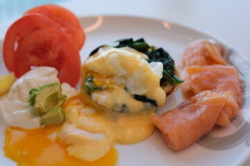 Hollandaise sauce, sauce for eggs Benedict liquid egg yolk running out. Two poached eggs on potato pancakes or toasted bread with tomatoes, fried onions and bacon with hollandaise sauce.