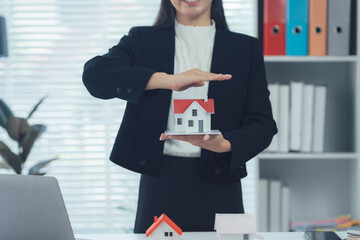 Protecting Dreams: A professional woman in a sharp suit cradles a miniature home, symbolizing the...