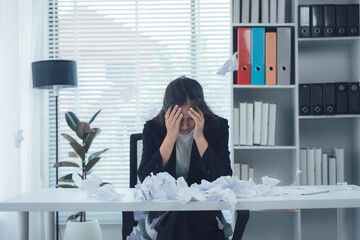 Overwhelmed at Work: A stressed individual sits amidst scattered paperwork, hand on head, embodying...