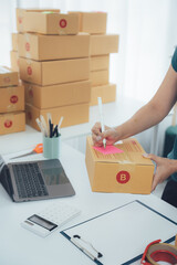 Fototapeta premium Package Preparation: A person meticulously prepares packages for shipment on a well-organized desk, with stacks of parcels and office supplies, readying orders for delivery. 
