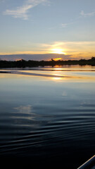 Serene sunset over Cuiaba River in the Pantanal wetlands with the golden sun. The sky is a beautiful gradient of orange and blue, with ripples in the foreground from a moving boat.