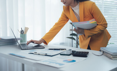 Businesswoman Working at Desk: A focused businesswoman, impeccably dressed in a vibrant suit,...
