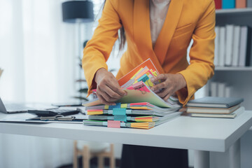 A businesswoman is working with a large pile of paperwork, searching for unfinished documents,...