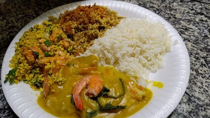 Closeup of a traditional Brazilian dish from Bahia, featuring shrimp Vatapá, a creamy sauce with dendê oil, served with shrimp farofa, another toasted farofa, and white rice on a plate.