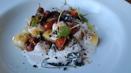 Gourmet Italian potato gnocchi served with a creamy white cheese sauce, roasted cherry tomatoes, black olive crumble, and fresh herbs. A beautifully plated dish from a fine dining restaurant.