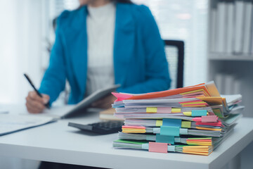 A businesswoman is working with a large pile of paperwork, searching for unfinished documents, information on piles of documents on her desk, and checking financial documents amidst her busy workload.