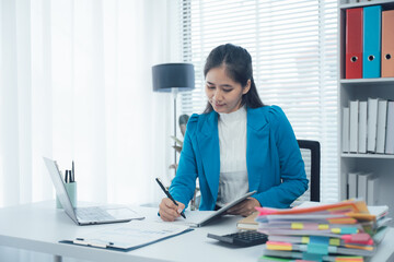 Focused Professional at Work: A determined businesswoman sits at her desk, engrossed in paperwork,...