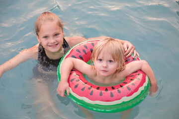Two kids enjoying a swim in the pool with a watermelon floatie