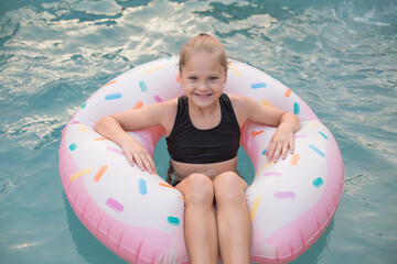 Smiling girl in a black swimsuit floating on a donut-shaped inflatable in a pool