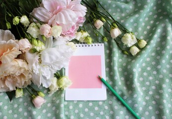 Flowers and notebook on green polka dot background. Top view