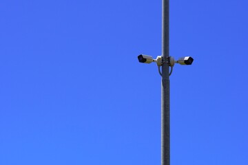 Metal pole with two CCTV cameras facing opposite directions against a clear blue sky - plenty of space for advertising, perfect for security or technology themes