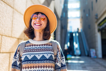 portrait of a stylish girl with a backpack in the city. happy young woman walking along the street...