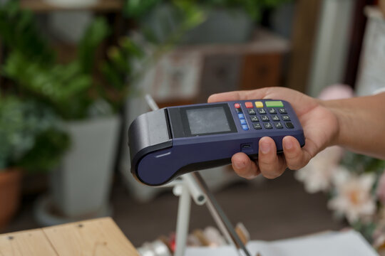 Male hand giving credit card to senior asian florist with card reader during payment in flower shop capturing real life contactless transaction in small floral business environment