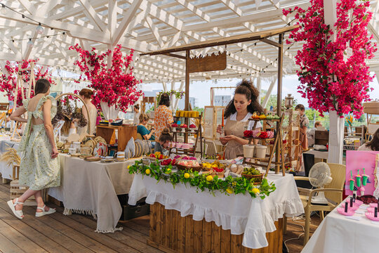 Female Artisan Standing Behind Stall with Handmade Fruit, Vegetable, and Dessert Shaped Candles at Artisan Market