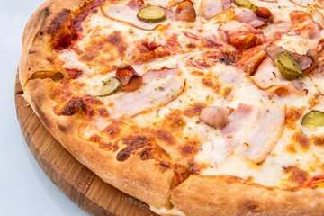 Delicious pizza topped with melted cheese, savory meats, and pickles, served on a wooden board, showcasing appetizing textures and vibrant colors for culinary delight