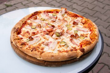 Delicious pizza topped with ham, pickles, and cheese, served on a wooden board, showcasing a mouthwatering dish perfect for sharing and enjoying with friends