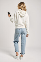 Young modern Model standing with phone in whit hoodie, talking and posing on white backdrop