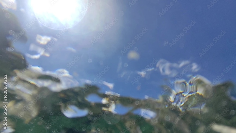 Aufkleber underwater point of view looking up at the bright sun and blue sky through the water's surface. the 