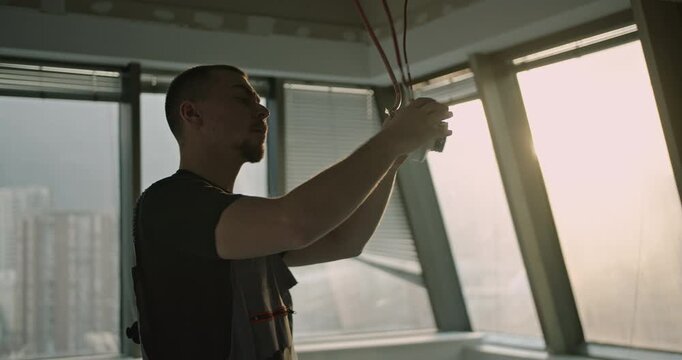 An electrician installs a smoke detector in an office building. He carefully connects the wires and ensures it's securely in place.