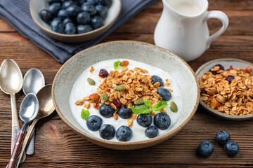 Healthy breakfast or snack meal, bowl of greek yogurt with blueberries and granola topping on a wooden table background