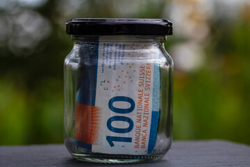 Swiss franc CHF banknote saving money in glass jar. Consumption and economy