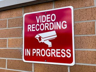 Video recording in progress warning sign. Video security camera surveillance signage on brick wall outside business location.