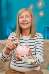 Caucasian mature woman saves money dollar cash by placing part of pension into into piggy bank...