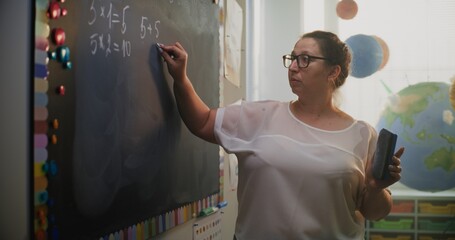 Female Teacher Writing on the Chalkboard, Talking to Students, Explaining Method of Multiplying...