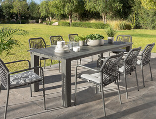 Idyllic outdoor dining set in a verdant garden, a sleek modern slate-gray aluminum table, stylish...