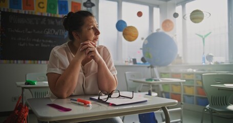 Tired Female Teacher Sitting Alone at the Desk in Empty Classroom, Relaxing After Class. Woman...