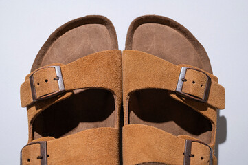 Brown sandals made of genuine leather on a cork sole on light gray background flat lay top view. Summer stylish fashion unisex shoes, beach and city casual footwear. Minimalistic shoes background