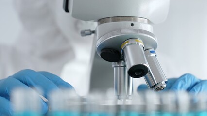 Scientific researcher or virologist wearing protective gear is tuning microscope lenses opposite...