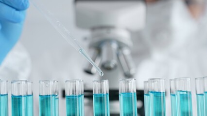 Close up of scientific researcher wearing protective gear, carefully pipetting liquid into test...