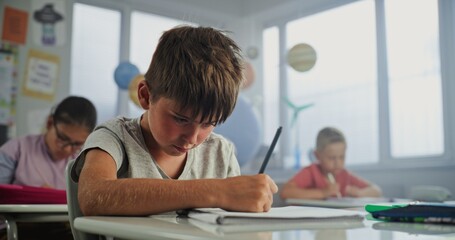 Elementary School Boy Sitting at Desk, Doing Writing Tasks in School Notebook. Team of Smart...