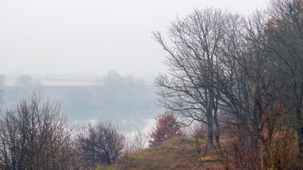 Panoramic view of an autumn river flowing through a misty landscape with trees on the banks reflection in the calm water