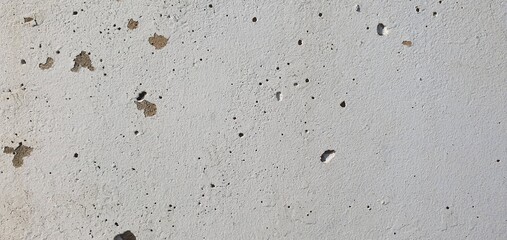 White painted concrete wall with small cracks, holes, and weathered surface, showing details of age, wear, and rough urban texture